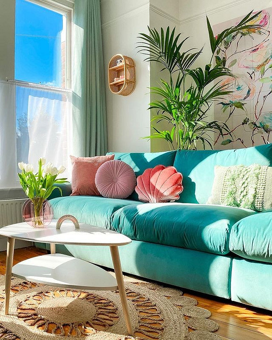 Дизайн вітальні з бірюзовим диваном, дерев'яною підлогою та килимом з геометричним візерунком.