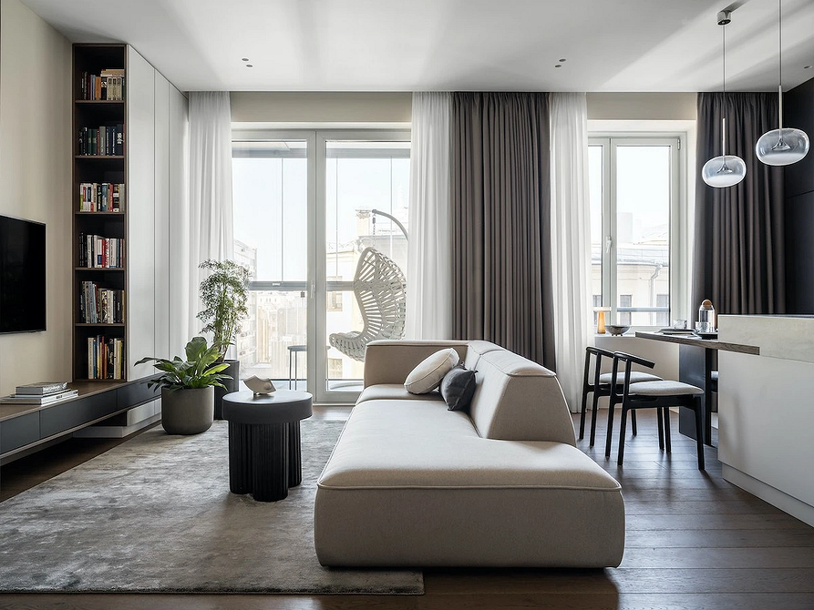 Монохромний сірий диван з декоративними рослинами у вітальні з великим вікном.