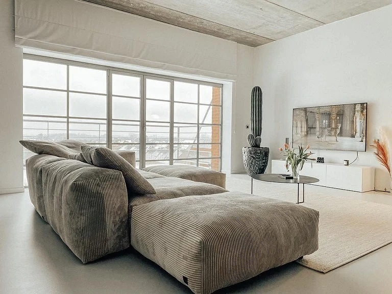 Світла вітальня з монохромним диваном, чорним торшером та акцентними деталями декору.