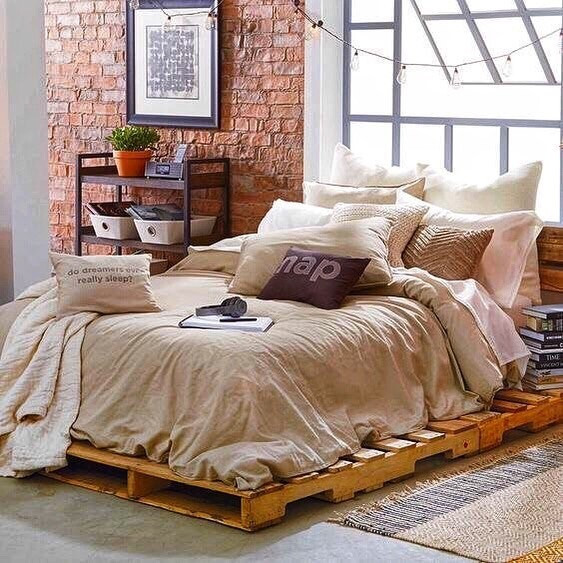 Ліжко з палет своїми руками у спальні з високим матрацом та подушками.