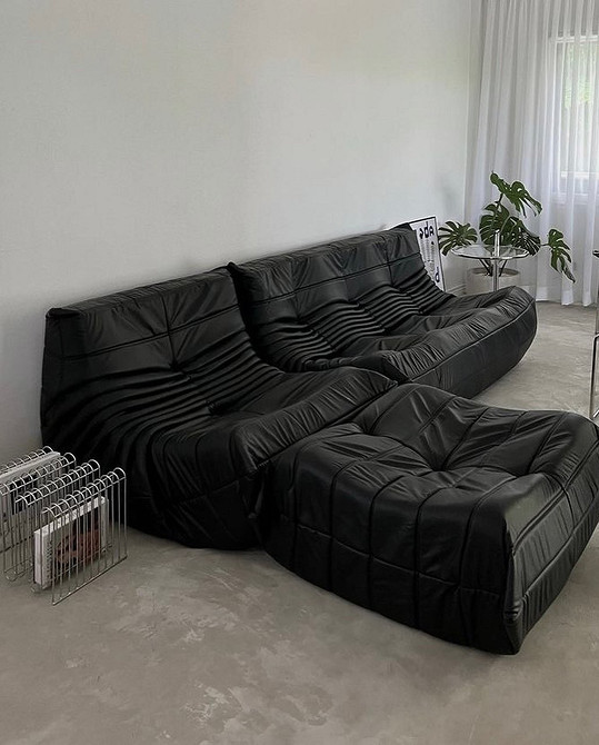 Кутовий шкіряний диван сірого кольору в сучасній вітальні з великими вікнами.