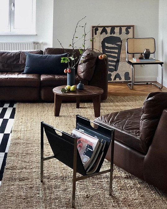 Кутовий шкіряний диван темного кольору у просторій вітальні з великими вікнами.