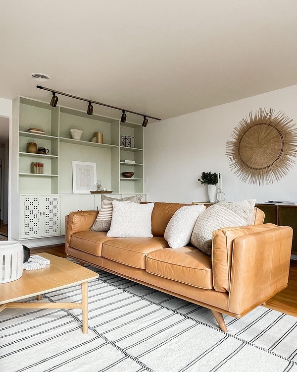 Стильний шкіряний диван коричневого кольору в інтер'єрі вітальні з килимом і подушками.