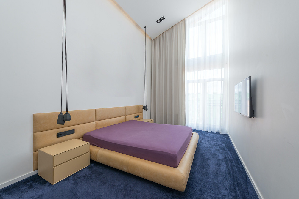 Стильна спальня з ліжком з м'яким узголів'ям з ґудзиками та текстильним декором для маленької квартири.