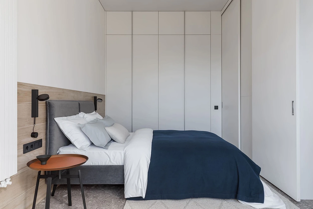 Сучасна спальня з сірим ліжком, великим дзеркалом та м'яким килимом на підлозі.