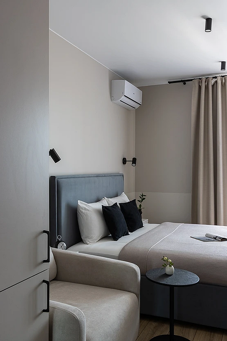 Стильна монохромна спальня з сірим ліжком, подушками та декоративною стіною.