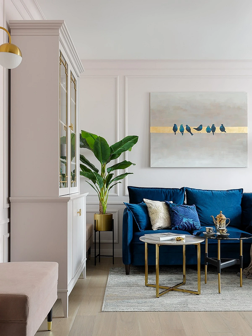 Синій диван у скандинавському стилі з дерев'яними ніжками в світлій вітальні.