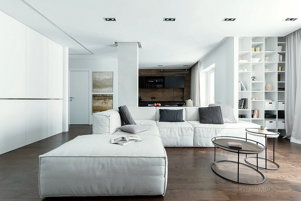 Світлий кутовий диван у кутку кімнати з великими вікнами, просторе та світле приміщення.