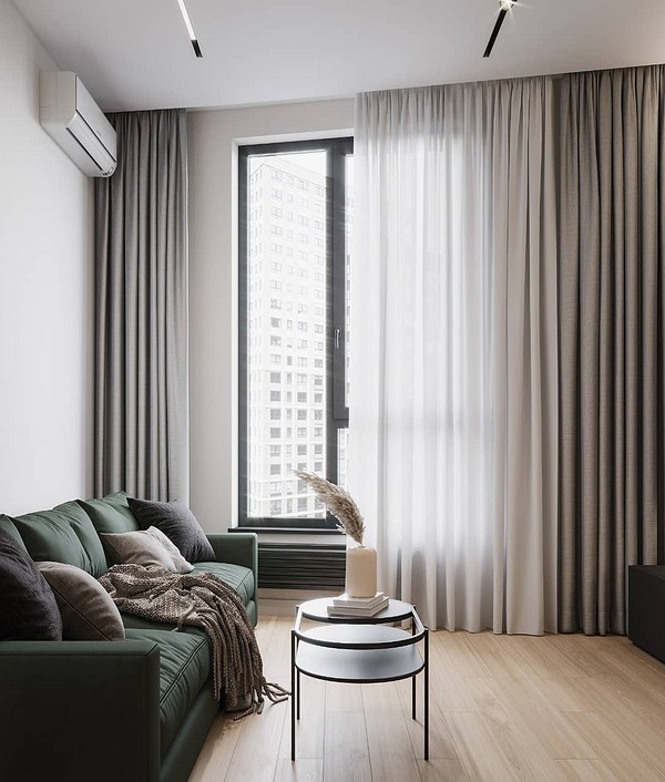 Зручний зелений диван у маленькій квартирі з яскравими подушками та пледом.