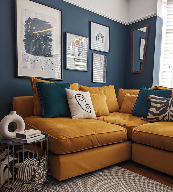 Жовтий кутовий диван в просторій вітальні з великими вікнами та зеленими рослинами.