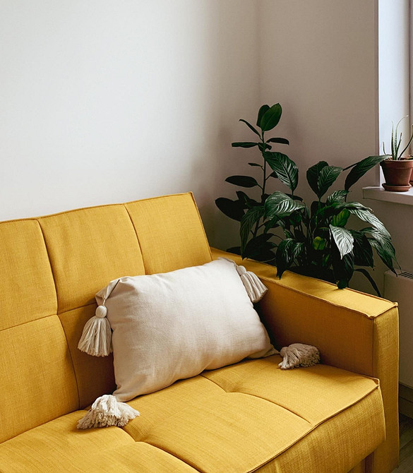 Жовтий диван у вітальні з великими вікнами і природним освітленням простору.