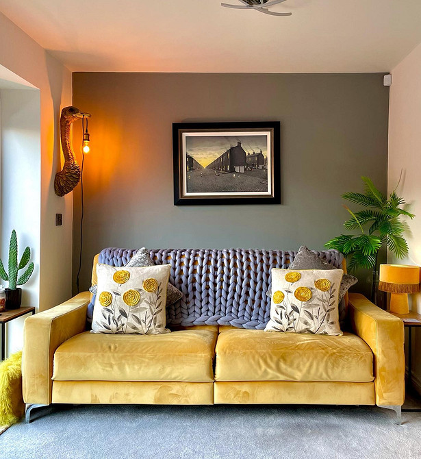 Жовтий диван у вітальні з сірими стінами та дерев'яною підлогою створює затишний простір.